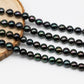 Beautiful near round peacock Tahitian Pearl in full strand display on top of a circle wood.