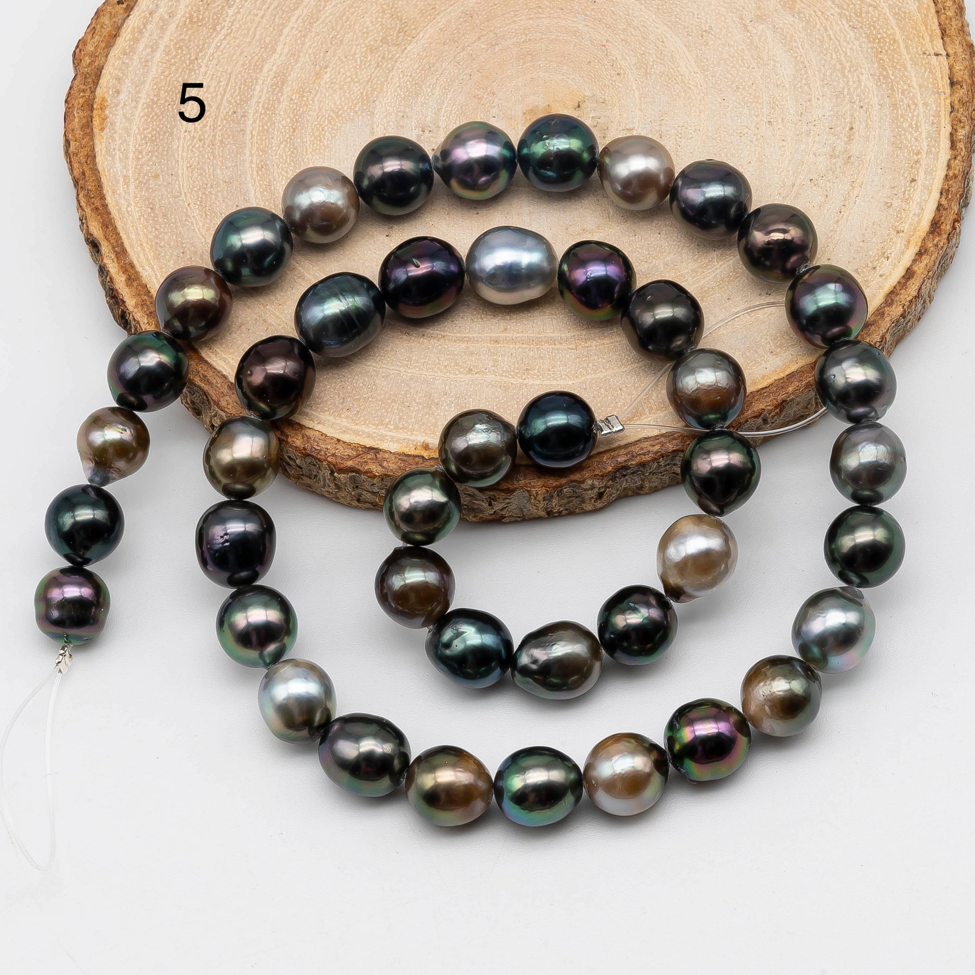 Full strand of Tahitian Pearl near round on top of the a circle wood displaying item number 5.