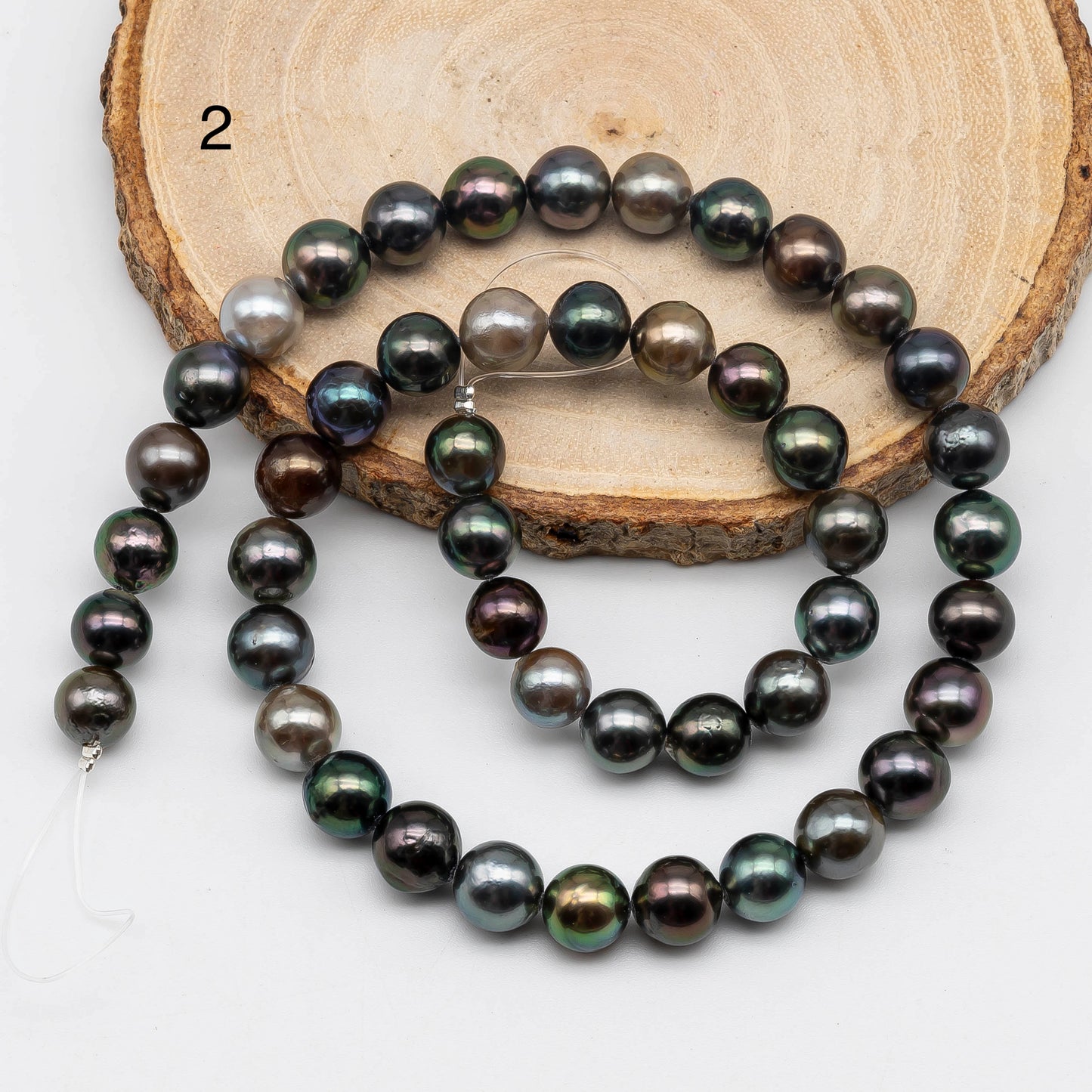 Tahitian Pearl near round in multi color strand. On top of the a circle wood displaying item number 2