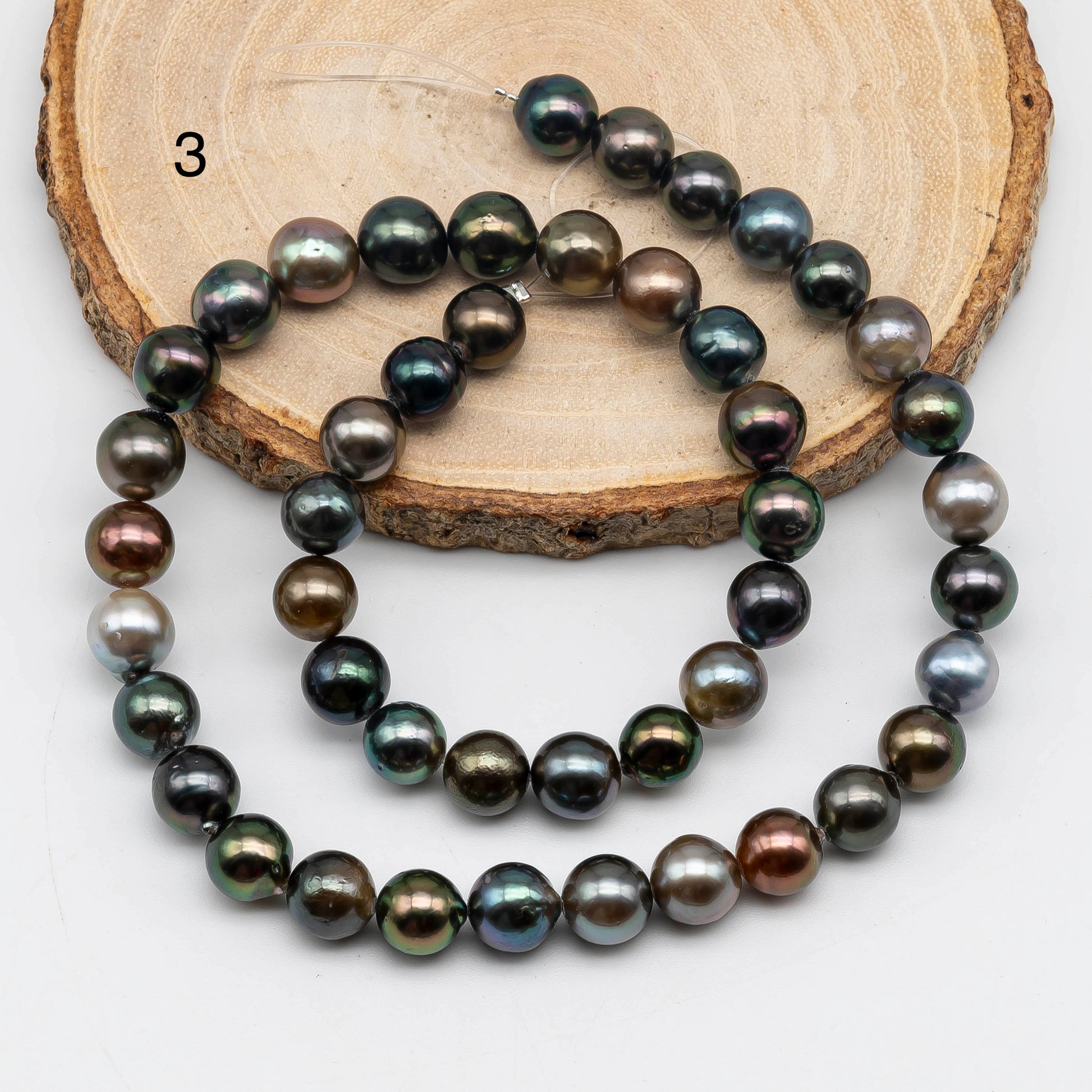 Near round Tahitian Pearl in multi color strand on top of the a circle wood displaying item number 3